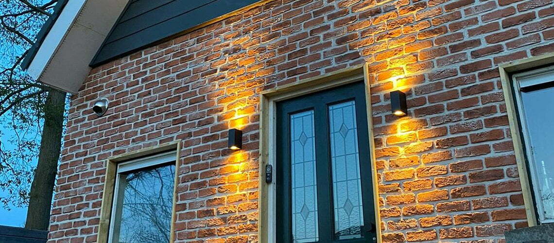 Een bakstenen gevel van 3d wandpanelen met verlichte wandlampen en een voordeur met glas-in-lood en een raam