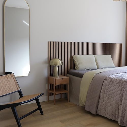 Een slaapkamer met een zithoek en een spiegel tegen een witte muur en akoestische panelen achter het bed