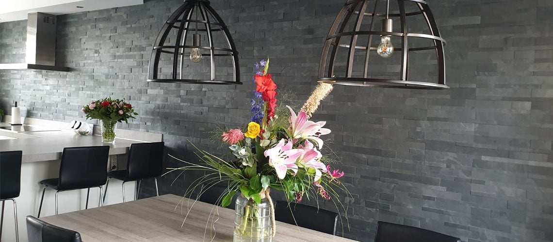 Grijze steenstrips muur in een kamer met industriële hanglampen en kleurrijke bloemstukken in een eetkamerhoek