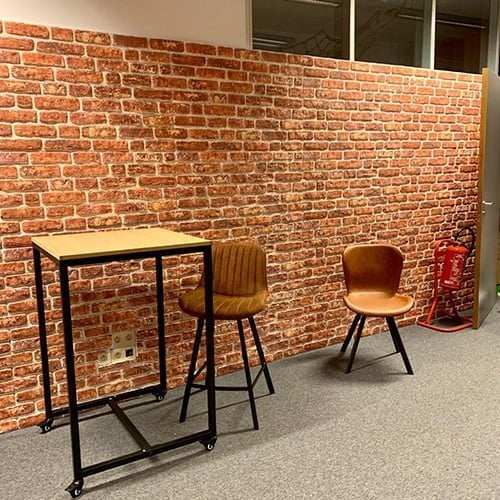 Een bakstenen 3d wandpanelen muur met hoge tafel bruine industriële stoelen en brandblusser
