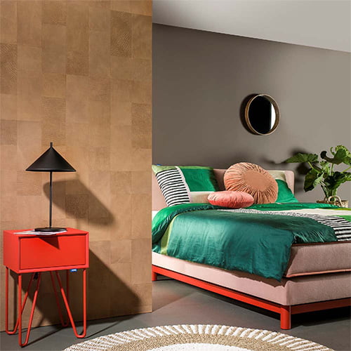 Slaapkamer met kleurrijk bed en rode bijzettafel naast beige leren wandtegels