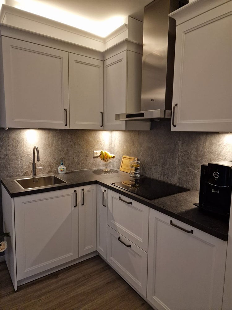 Moderne keuken met witte keukenkasten en donkere werkbladen met geïntegreerde verlichting