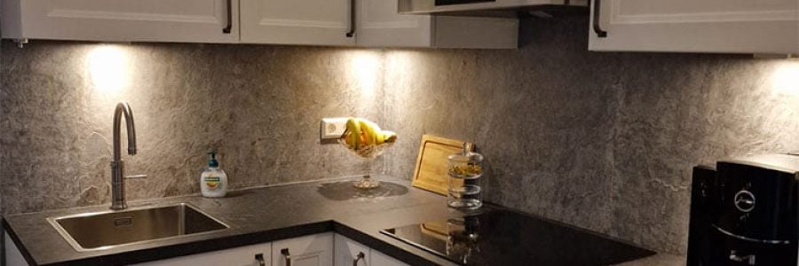 Moderne-witte-keuken-met-achterwand.jpg Moderne keuken met witte keukenkasten en donkere werkbladen met geïntegreerde verlichting