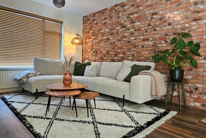 PU baksteen barok dark rustic rood woonkamer Woonkamer met industriële bakstenen muur, lichtgrijze bank, houten tafels en vloerkleed