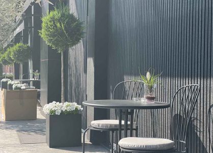 Terras met zwarte kunststof gevelbekleding en groenblijvende planten en ronde tafel