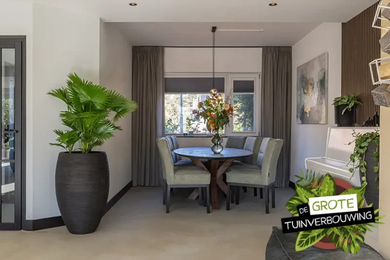 Stijlvolle eetkamer met ronde houten tafel, groene stoelen en grote kamerplant naast de witte piano, in een natuurlijk verlichte ruimte