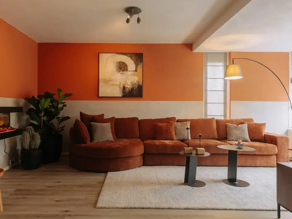 Moderne woonkamer met oranje accentmuur en beton cire wandpanelen in natuurlijke kleur.
