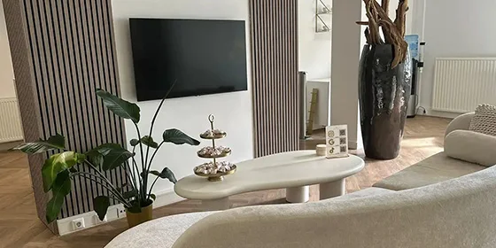 Stijlvolle TV-wand met verticale akoestische wandpanelen in houtlook, gecombineerd met zachte beige meubels, een moderne salontafel en kamerplant in een licht, modern interieur.