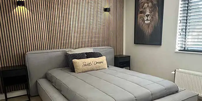 Slaapkamer met houten akoestische wandpanelen achter grijs gestoffeerd bed, modern interieur met kunstwerk van leeuw en zwarte nachtkastjes