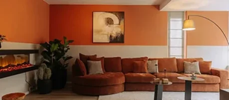 Gezellige woonkamer met warme terracotta lambrisering, een grote fluwelen hoekbank, een elektrische haard en sfeervolle verlichting