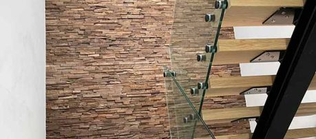 Trap met houtstrips en glazen balustrade tegen een stenen muur
