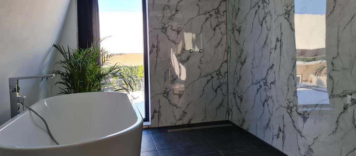 Ruime badkamer met vrijstaand bad marmer wandpanelen grote glazen douche en uitzicht naar buiten