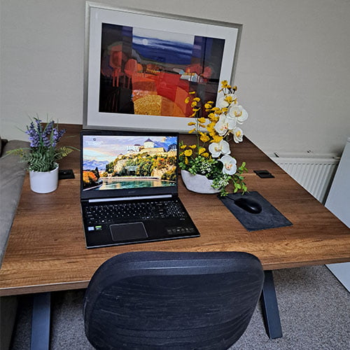 Duurzame thuiswerkplek met houten bureau, laptop, bloemen en kunstwerk op het bureau