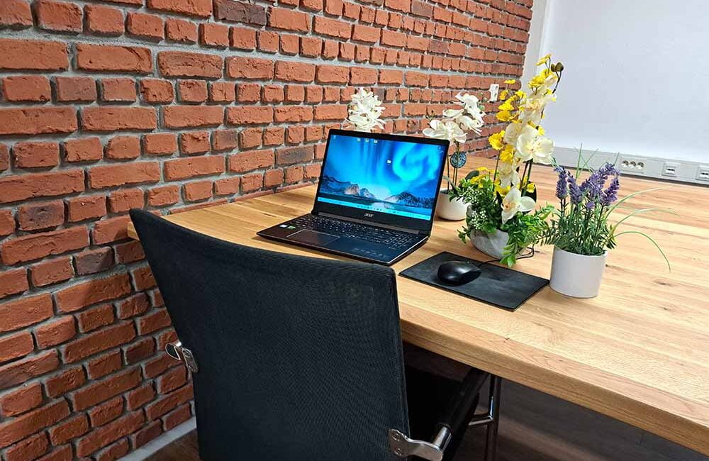 Thuiswerkplek met laptop op een bureau, versierd met planten en een bakstenen muur als achtergrond