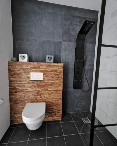 Badkamer met donkere tegels, houten accentmuur en zwarte douche