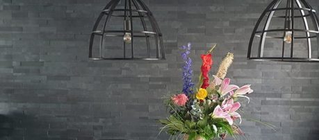 Grijze steenstrips wandbekleding met kleurrijk bloemstuk en industriële lampen