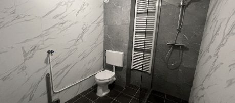 Badkamer met toegankelijke voorzieningen zoals grijze zelfklevende tegel wandbekleding en douche